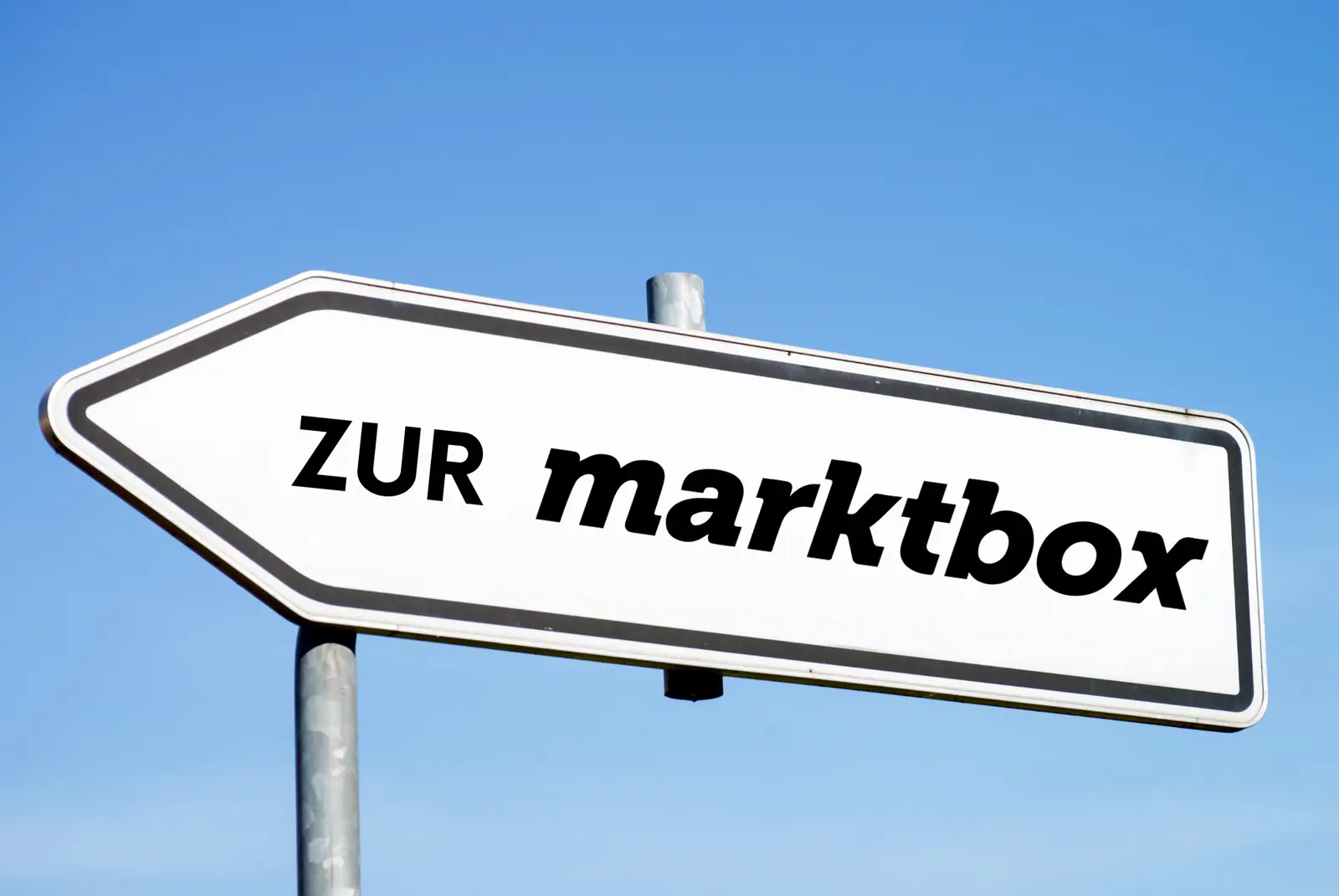 Weißes Pfeilschild mit der Aufschrift „ZUR marktbox“ vor blauem Himmel, das nach links zeigt