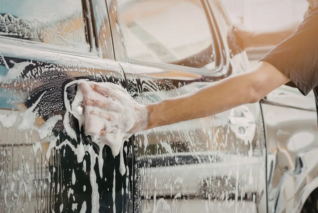 Hand wäscht eine dunkle Autotür mit viel weißem Reinigungsschaum