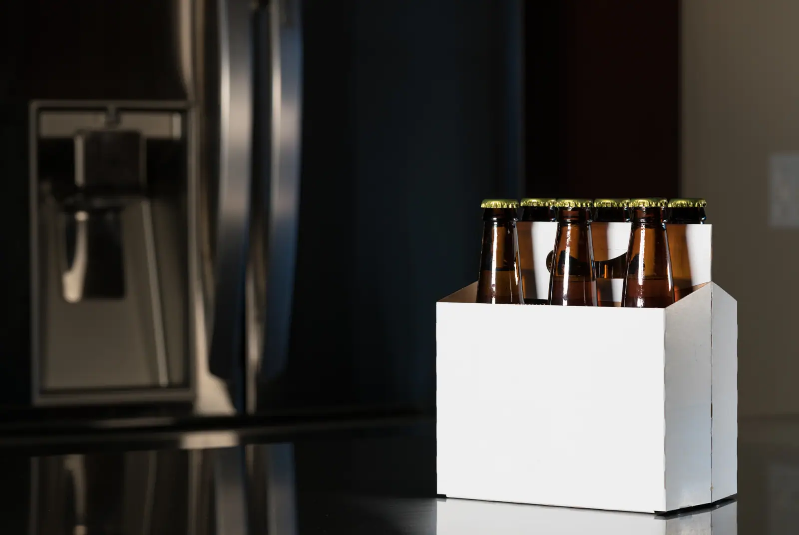 Sechs braune Bierflaschen in einem neutralen weißen Sechserträger auf einer dunklen Oberfläche