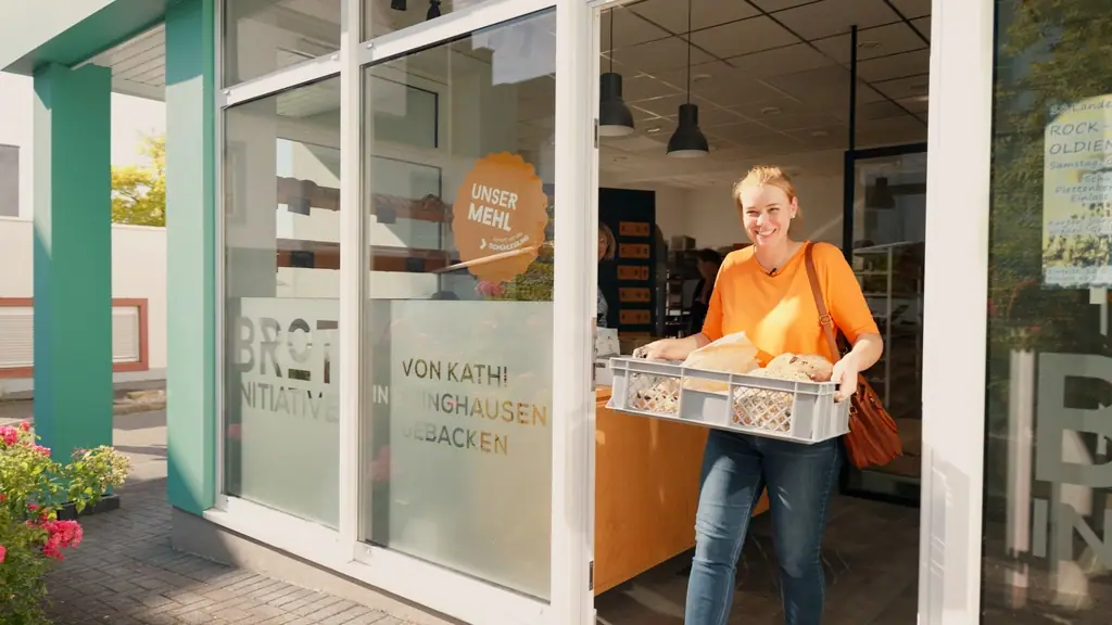 Lächelnde Frau trägt eine Kiste mit frischem Brot aus dem Eingangsbereich einer Bäckerei