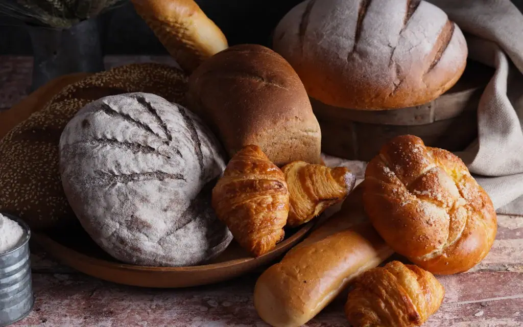Auswahl an frisch gebackenen Broten, Brötchen und goldbraunen Croissants auf einer rustikalen Holzunterlage