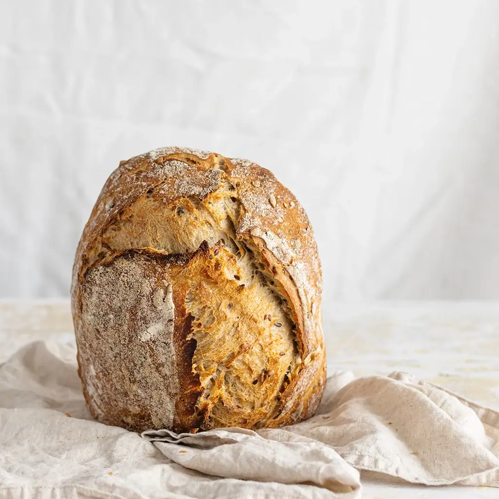 Rustikaler Laib Brot mit knuspriger Kruste und Körnern auf einem hellen Leinentuch