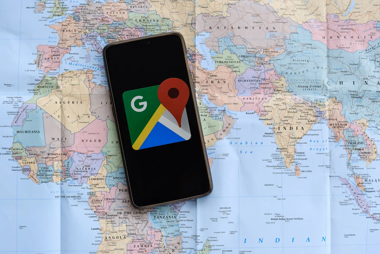 Smartphone mit dem Google-Maps-Logo auf einer ausgebreiteten Weltkarte