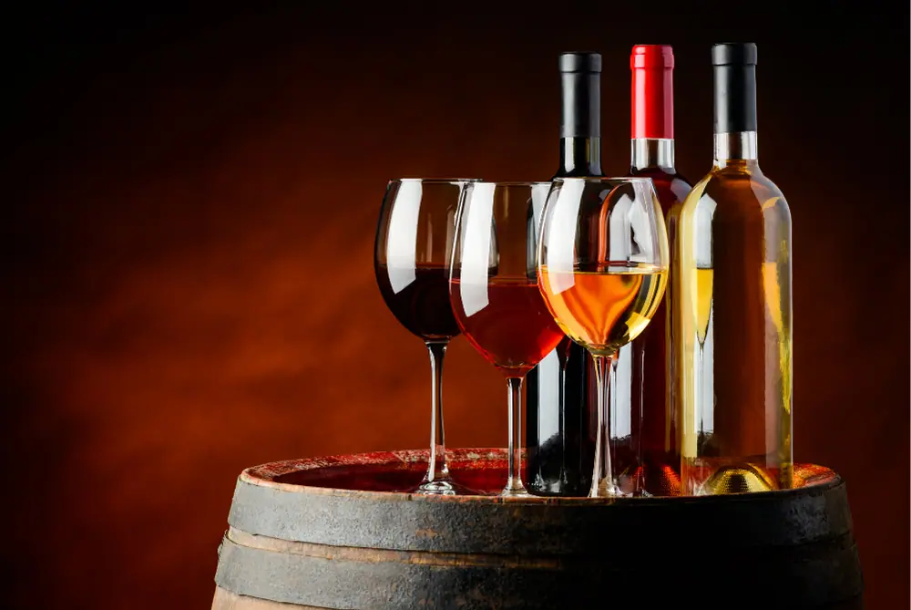 Drei Gläser und Flaschen mit Rot-, Rosé- und Weißwein stehen auf einem rustikalen Holzfass
