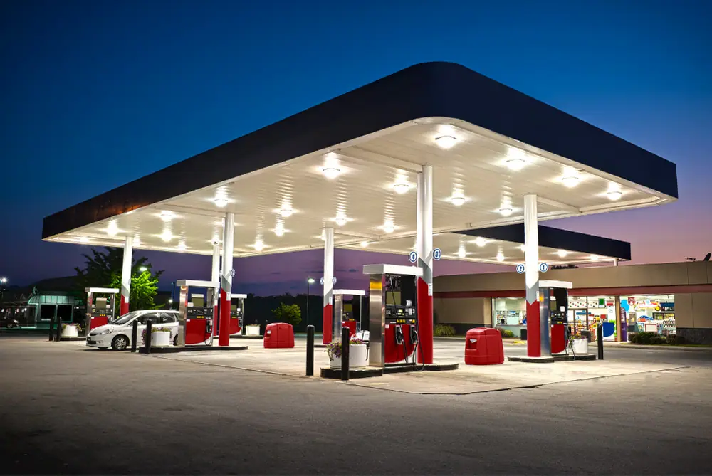Beleuchtete Tankstelle bei Dämmerung mit Zapfsäulen unter einem großen Dach und einem angrenzenden Shop