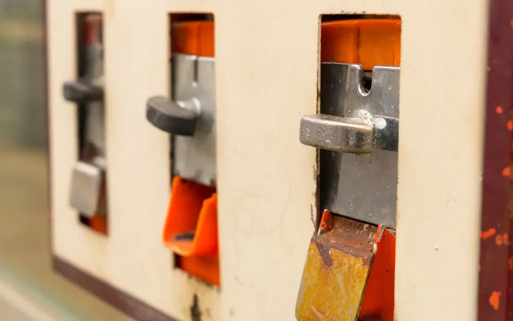 Drei mechanische Warenautomaten mit Metallhebeln und Rostspuren an orangefarbenen Ausgabefächern