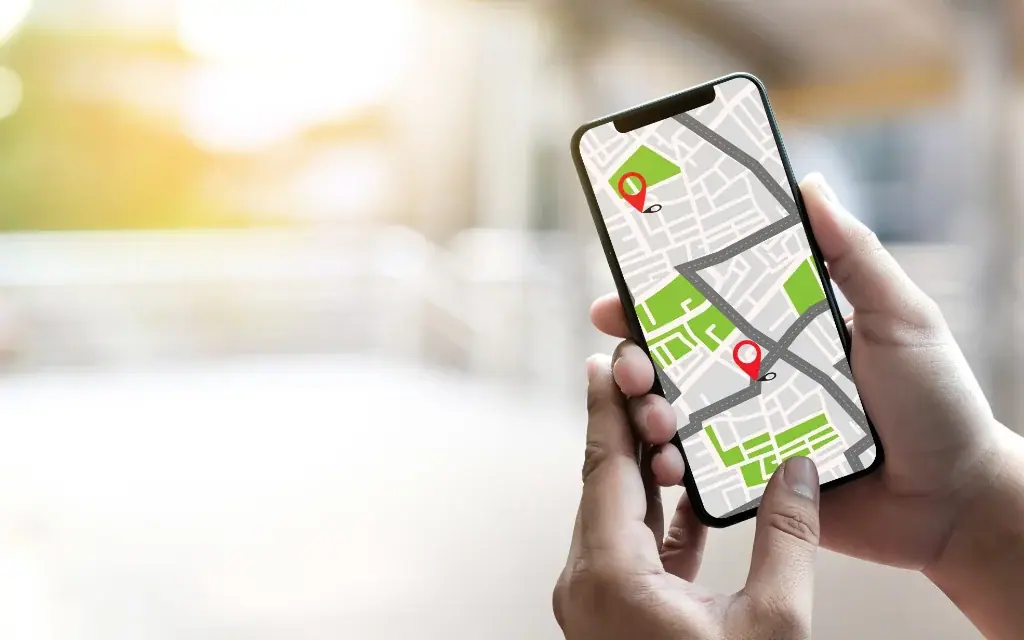 Hände halten ein Smartphone mit einer digitalen Karte und roten Standort-Pins vor einem hellen Hintergrund