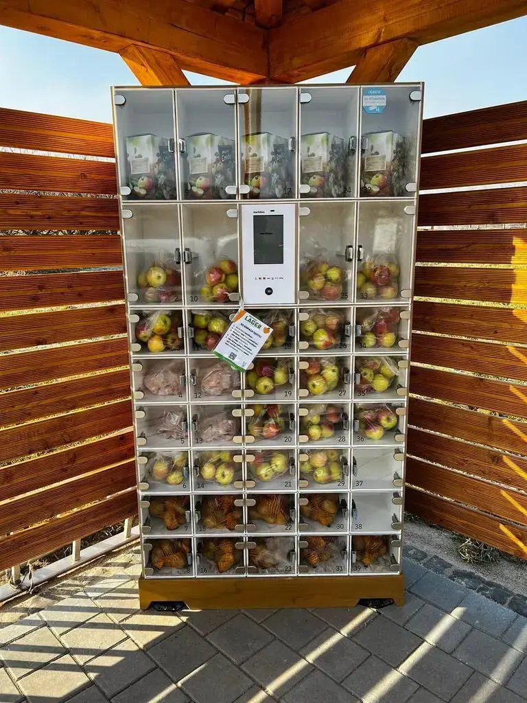 Verkaufsautomat marktbox mit Glasfächern voller Äpfel, Säfte und Kartoffeln in einer hölzernen Schutzhütte