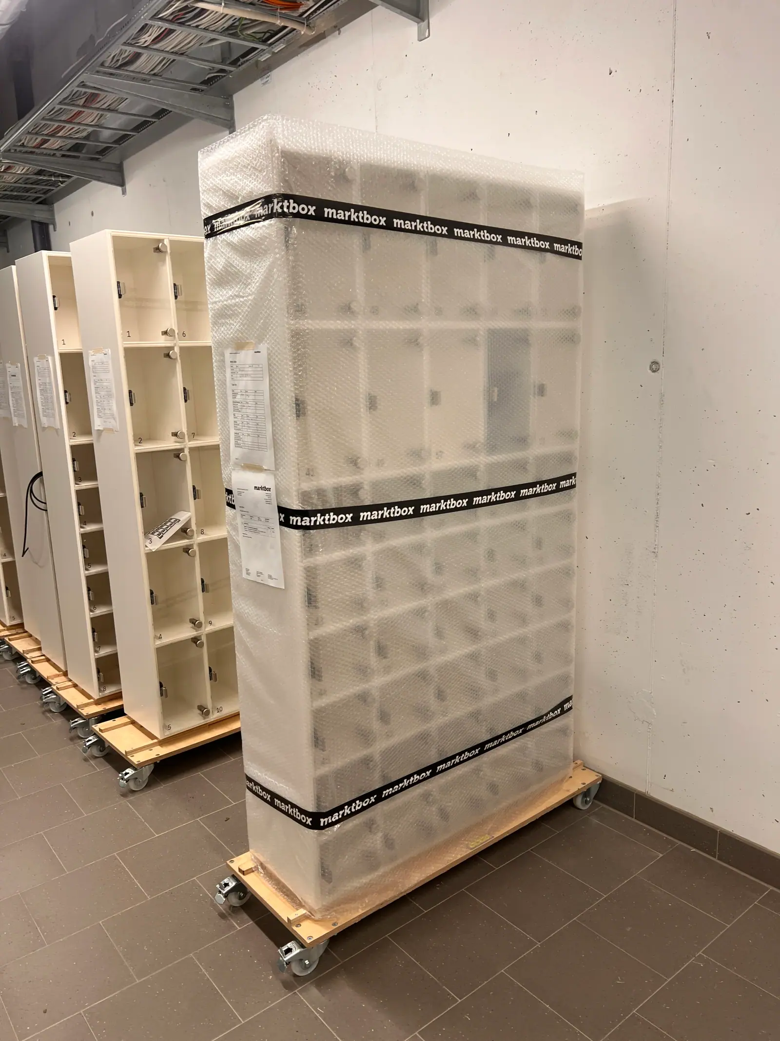 Weiße Marktbox-Module auf Rollwagen, eines davon transportfertig in Luftpolsterfolie verpackt