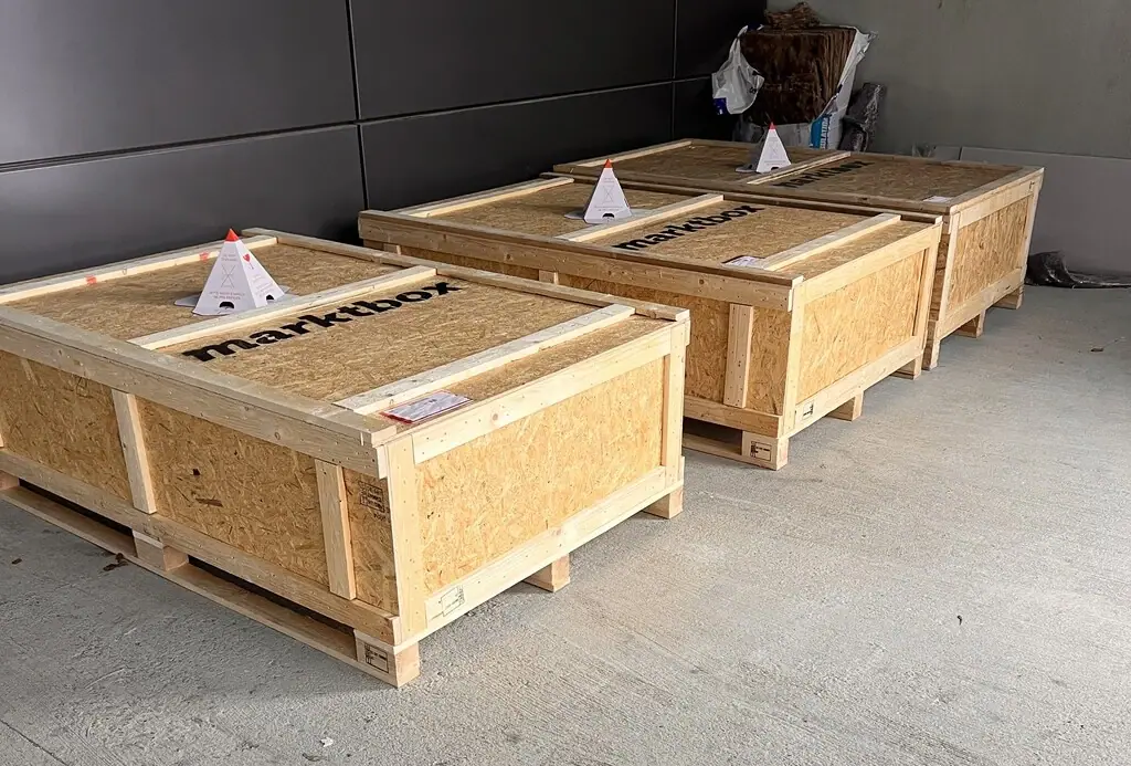 Drei mit dem marktbox-Logo beschriftete Holzkisten stehen auf Paletten in einer Lagerhalle
