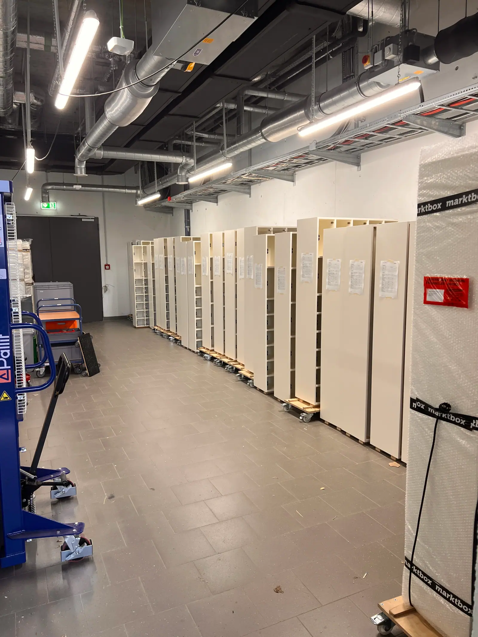 Mehrere weiße marktbox-Automaten stehen in einer Reihe auf Rollwagen in einer Lagerhalle bereit