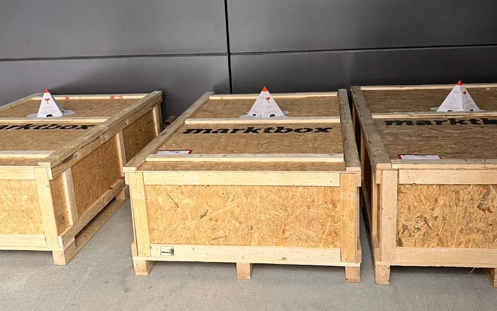 Drei große Holzkisten mit marktbox-Logo stehen nebeneinander für den Versand bereit